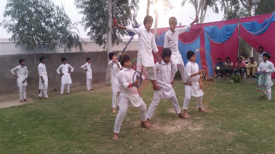 Students in white kurta-pyjama performing Gatka with sticks on the school lawn