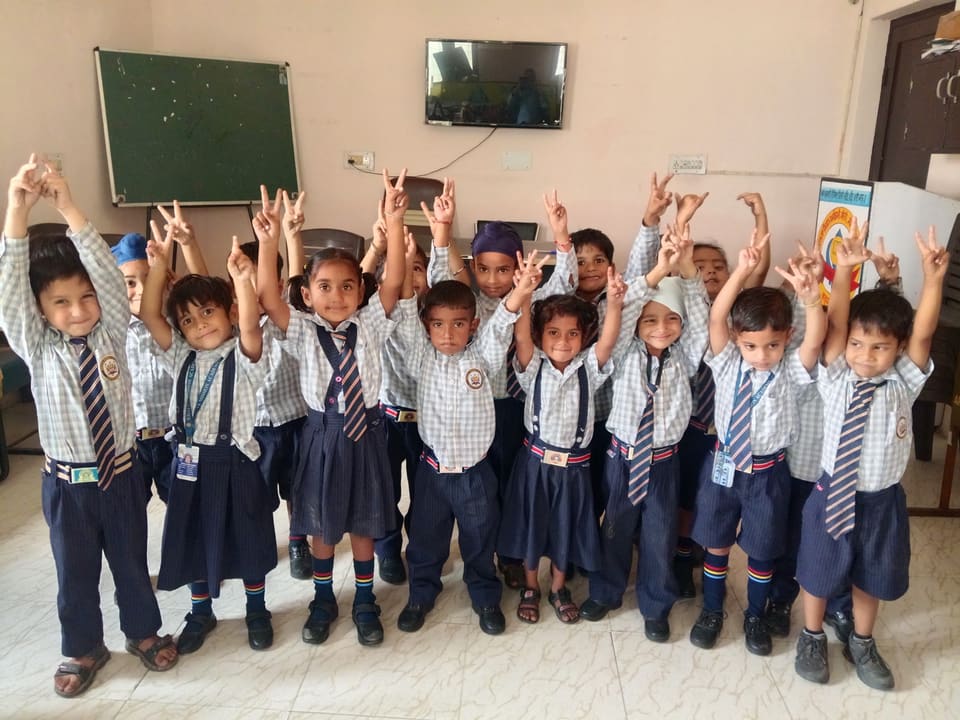 Kindergarten students in uniform with hands raised in class
